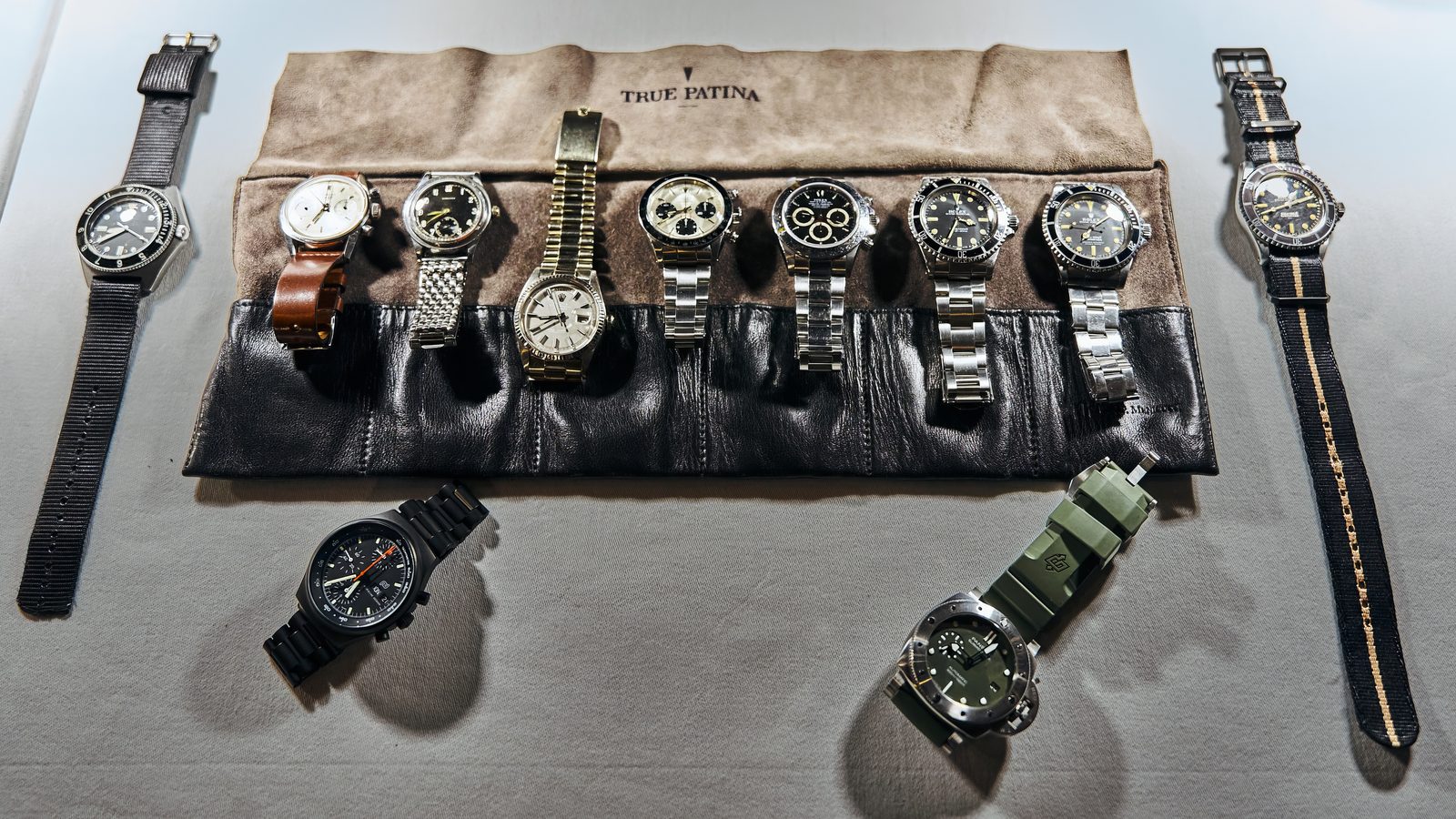 A row of watches on a leather watch roll on a white tablecloth